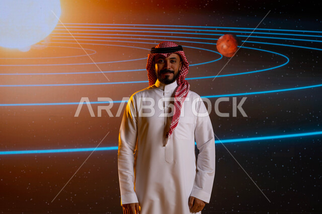 رجل اعمال سعودي عربي خليجي يقف امام شاشة الكترونية حديثة، رحلة السعودية نحو الفضاء الخارجي، ايماءات وجه تدل على السعادة، نمو وتطوير قطاع الفضاء في السعودية، خلفية شاشة عرض لمسار حركة الارض والكواكب حول الشمس، رؤية مستقبلية 2030