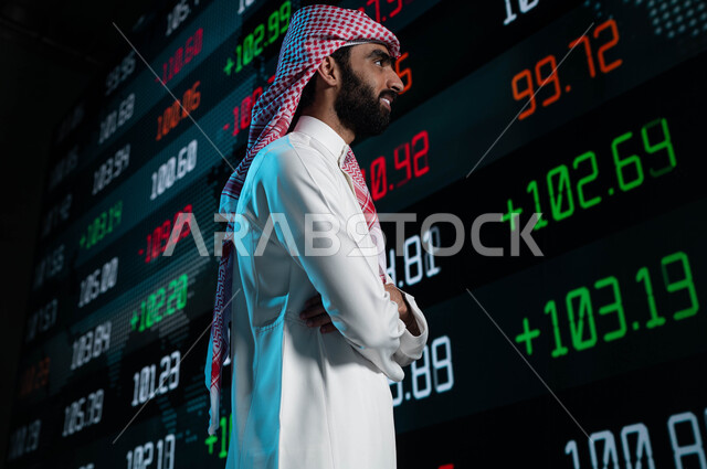 متابعة الأسهم السعودية من خلال شاشات الكترونية حديثة، رجل أعمال عربي خليجي سعودي يقف أمام شاشات سوق الأوراق المالية، تحليل البيانات والمعلومات ذات الطبيعة الرقمية، الإستثمار في البورصة السعودية، خلفية شاشة عرض للأسهم المتداول بها في السعودية