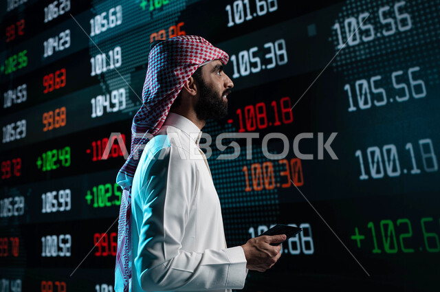 شاشة عرض للأسهم المتداول بها في السعودية، رجل أعمال عربي خليجي سعودي يقف أمام شاشات تداول الأسهم ويستخدم التابليت في تحليل البيانات والمعلومات ذات الطبيعة الرقمية، الإستثمار في البورصة السعودية، متابعة سوق الأوراق المالية من خلال شاشات الكترونية حديثة