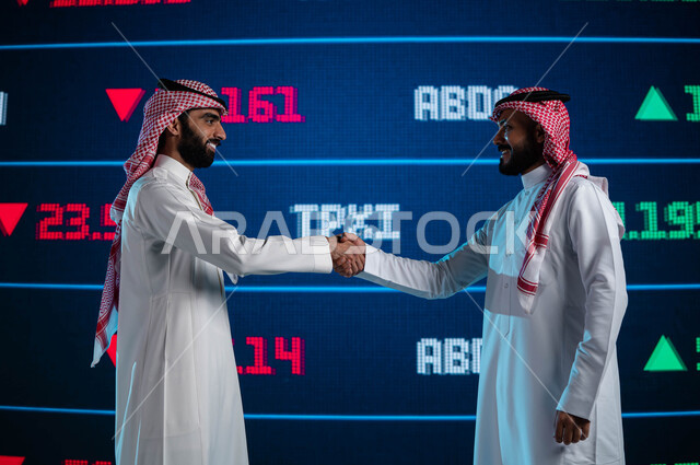 الإستثمار في البورصة السعودية، رجلان اعمال سعوديان عربيان خليجيان يتصافحان، صفقة عمل وتعاقدات واتفاقيات اقتصادية سعودية ناجحة، شاشة إلكترونية حديثة لعرض الأسهم المتداول بها في السعودية، خلفية شاشة البيانات والمعلومات ذات الطبيعة الرقمية