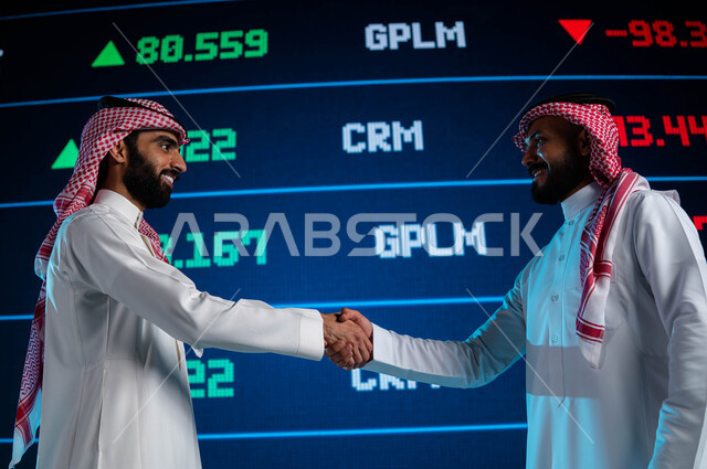 صفقة عمل وتعاقدات واتفاقيات اقتصادية سعودية ناجحة، رجلان اعمال سعوديان عربيان خليجيان يتصافحان، شاشة إلكترونية حديثة لعرض الأسهم المتداول بها في السعودية، الإستثمار في البورصة السعودية، خلفية شاشة البيانات والمعلومات ذات الطبيعة الرقمية