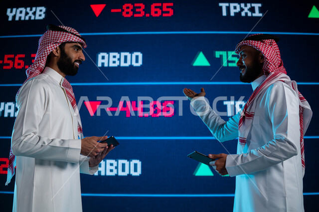 متابعة سوق الاوراق المالية، رجلان أعمال سعوديان خليجيان عربيان يستخدمان التابليت ويتناقشان في البيانات والمعلومات الرقمية للأسهم السعودية، الإستثمار المالي والإقتصادي في البورصة السعودية، شاشة إلكترونية حديثة تظهر الأسهم المتداول بها في السعودية