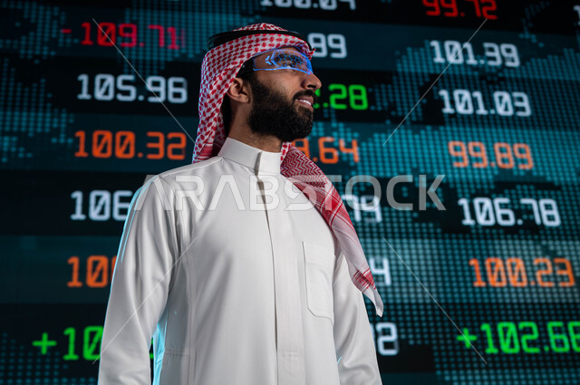 متابعة الأسهم المتداول بها في السعودية من خلال شاشات الكترونية حديثة، رجل اعمال عربي خليجي سعودي يرتدي نظارات الواقع الافتراضي، الإستثمار المالي والإقتصادي في البورصة السعودية، تحليل البيانات والمعلومات الرقمية، خلفية شاشة عرض رقمية للأسواق المالية