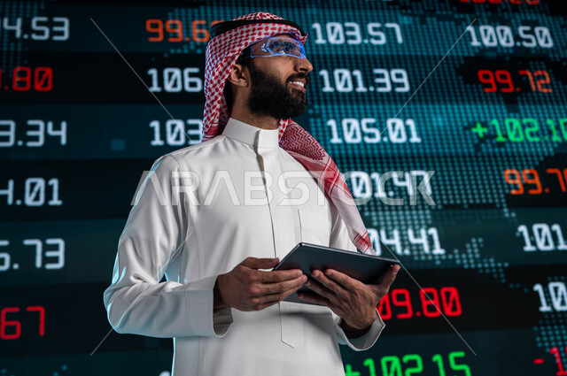 الإستثمار المالي والإقتصادي في البورصة السعودية، استخدام التابليت في تحليل البيانات والمعلومات ذات الطبيعة الرقمية، رجل اعمال عربي خليجي سعودي يرتدي نظارات الواقع الافتراضي، متابعة الأسهم المتداول بها في السعودية من خلال شاشات الكترونية حديثة
