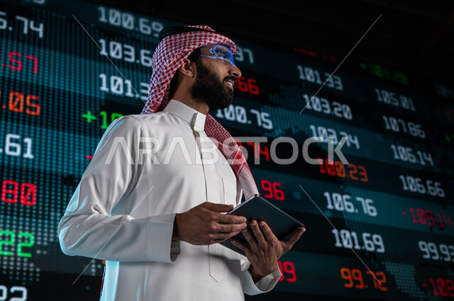 استخدام التابليت في تحليل البيانات والمعلومات ذات الطبيعة الرقمية، رجل اعمال عربي خليجي سعودي يرتدي نظارات الواقع الافتراضي، الإستثمار المالي والإقتصادي في البورصة السعودية، متابعة الأسهم المتداول بها في السعودية من خلال شاشات الكترونية حديثة