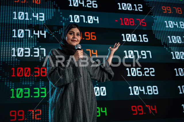 خلفية شاشات الكترونية حديثة لمتابعة السوق السعودي، سيدة اعمال خليجية سعودية عربية تمسك المايكروفون وتتحدث في مؤتمر اقتصادي، ندوات اقتصادية سعودية، مقترحات ونصائح حول التدوال الإلكتروني، عرض تقديمي لأخبار أسهم الشركات في البورصة السعودية
