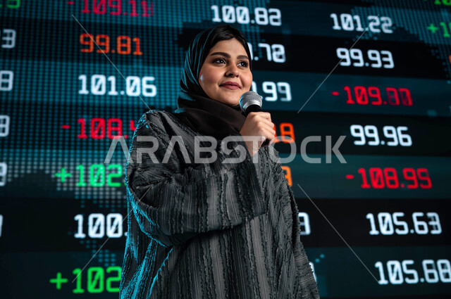 Suggestions and tips about electronic trading, a Saudi Arabian Gulf businesswoman holding a microphone and speaking at an economic conference, Saudi economic seminars, a presentation of company stock news on the Saudi Stock Exchange, a background of moder