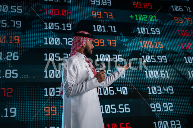 ندوات اقتصادية سعودية، خلفية شاشات الكترونية حديثة لمتابعة السوق السعودي، رجل اعمال خليجي سعودي عربي يمسك المايكروفون ويتحدث في مؤتمر اقتصادي، مقترحات ونصائح حول التدوال الإلكتروني، عرض تقديمي لأخبار أسهم الشركات في البورصة السعودية