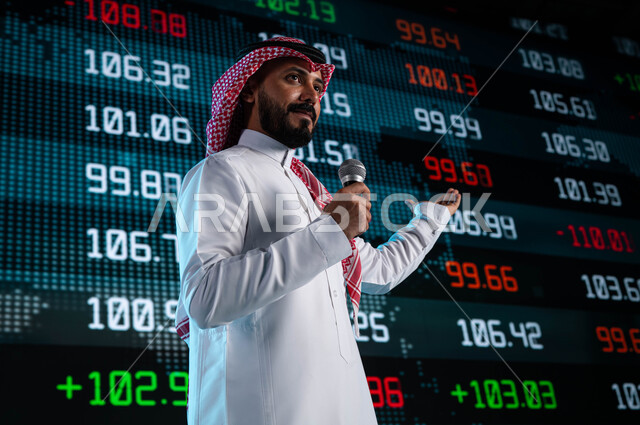 عرض تقديمي لأخبار أسهم الشركات في البورصة السعودية، خلفية شاشات الكترونية حديثة لمتابعة الأسهم المتداول بها في السعودية، رجل اعمال خليجي سعودي عربي يمسك المايكروفون ويتحدث في مؤتمر اقتصادي سعودي، مقترحات ونصائح حول التدوال الإلكتروني