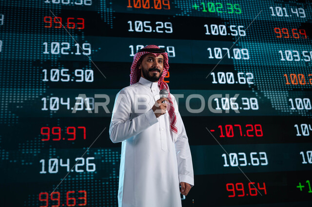 مقترحات ونصائح حول التدوال الإلكتروني، خلفية شاشات الكترونية حديثة لمتابعة البيانات والمعلومات ذات الطبيعة الرقمية، رجل اعمال خليجي سعودي عربي يمسك المايكروفون ويتحدث في مؤتمر اقتصادي سعودي، عرض تقديمي لأخبار أسهم الشركات في البورصة السعودية