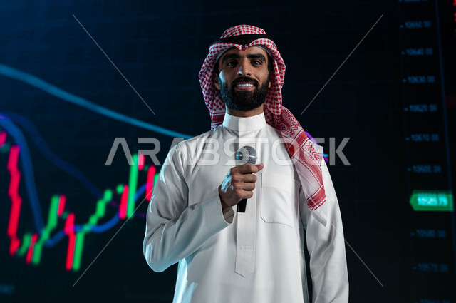 عرض تقديمي لأخبار أسهم الشركات في البورصة السعودية، رجل اعمال خليجي سعودي عربي يمسك المايكروفون ويتحدث في مؤتمر اقتصادي سعودي، مقترحات ونصائح حول التدوال الإلكتروني، خلفية شاشات الكترونية حديثة لمتابعة صعود وهبوط مؤشر البورصة