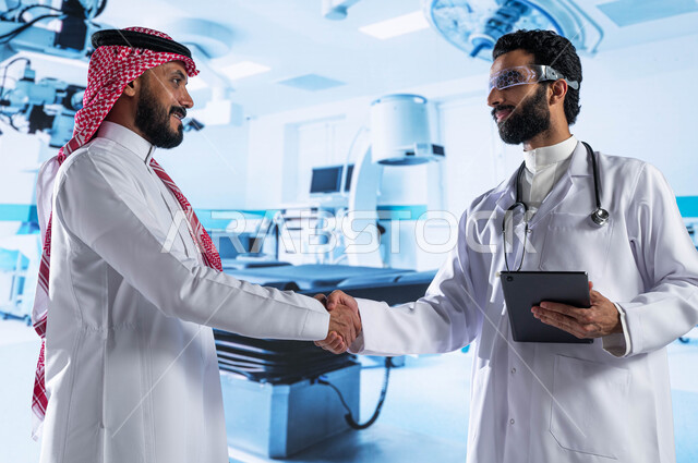 معدات وأجهزة طبية إلكترونية متطورة في المستشفيات والمراكز الحديثة، طبيب عربي سعودي خليجي يرتدي المعطف الأبيض ونظارة الواقع الإفتراضي ويحمل بيده جهاز التابلت ويقوم بمصافحة رجل يرتدي الزي السعودي، تعاقدات واتفاقيات عمل طبية سعودية ناجحة، رؤية مستقبلية 2030