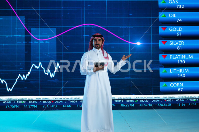 قراءة الموجز الأخباري بإستخدام جهاز التابلت، مذيع وإعلامي عربي خليجي سعودي يقوم بتقديم النشرات الإخبارية الإقتصادية، التغيرات الحاصلة في أسعار السلع والثروات، خلفية شاشة إلكترونية حديثة لصعود وهبوط مؤشر الأسهم والبورصة