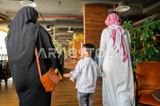 صورة من الخلف لعائلة عربية خليجية سعودية تقوم بمغادرة المطعم ،  قضاء وقتا ممتعا في المطعم ، قضاء أوقات عائلية ترفيهية ، قضاء العطلة مع العائلة ، جلسات فريدة و مميزة ، مطاعم و كافيهات في السعودية