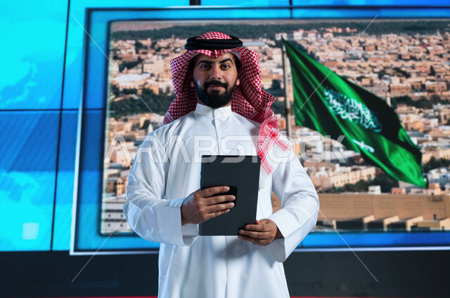 دمج البيئة العملية مع التقنية والتكنولوجيا، مذيع عربي سعودي خليجي يقوم بقراءة الموجز الإخباري بإستخدام التابليت، تقديم النشرة الإخبارية، الإحتفال بيوم العلم السعودي وإحياء ذكرى اليوم الوطني، خلفية شاشة إلكترونية لمدن ومعالم السعودية