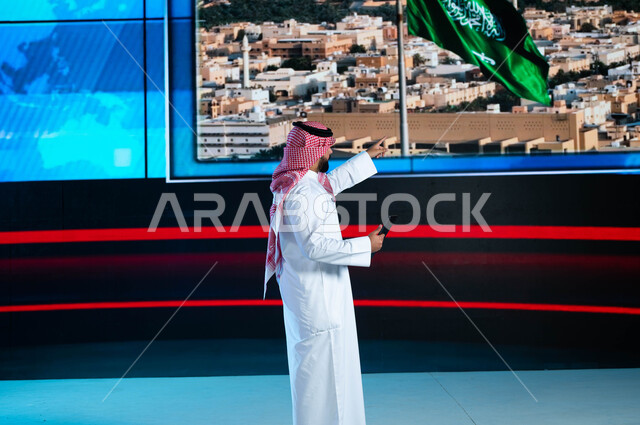 خلفية شاشة إلكترونية لمدن ومعالم السعودية، قراءة الموجز الإخباري بإستخدام التابليت، الإحتفال بيوم العلم السعودي وإحياء ذكرى اليوم الوطني، مذيع عربي سعودي خليجي يقوم بتقديم النشرة الإخبارية، دمج البيئة العملية مع التقنية والتكنولوجيا