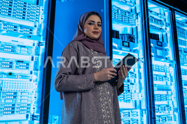 غرفة التحكم بالسيرفرات وخوادم الانترنت، امرأة عربية خليجية سعودية تقوم بالتحكم بالمواقع المستضافة على السيرفرات من خلال جهاز التابلت، تسهيل الوصول للمعلومات من خلال نظم قواعد البيانات، خلفية هولوجرامية ثلاثية الأبعاد لمركز البيانات