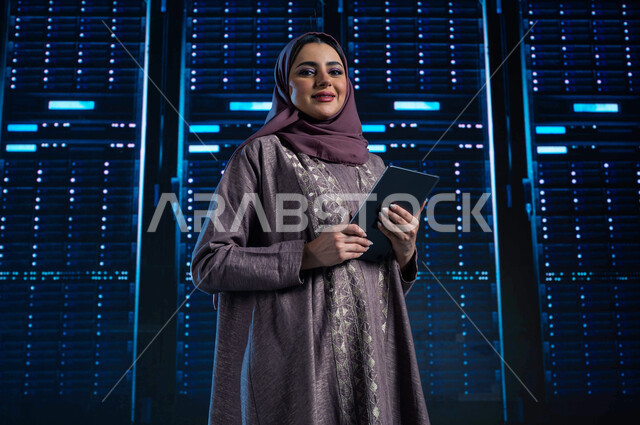 خلفية هولوجرامية ثلاثية الأبعاد لمركز البيانات، تسهيل الوصول للمعلومات من خلال نظم قواعد البيانات، امرأة عربية خليجية سعودية تقوم بالتحكم بالمواقع المستضافة على السيرفرات من خلال جهاز التابلت، غرفة التحكم بالسيرفرات وخوادم الإنترنت