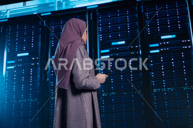 إستثمار الخبرات السعودية في بناء مراكز بيانات متطورة وحديثة، امرأة عربية خليجية سعودية تستخدم جهاز التابليت في الإشراف وإدارة معلومات الداتا سنتر، شبكة التخزين السحابي، خلفية هولوجرامية ثلاثية الأبعاد لغرفة التحكم بالسيرفرات وخوادم الانترنت