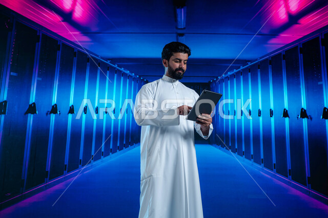 إستثمار الخبرات السعودية في بناء مراكز بيانات متطورة وحديثة، شبكة التخزين السحابي، خلفية هولوجرامية ثلاثية الأبعاد لغرفة التحكم بالسيرفرات وخوادم الانترنت، رجل عربي خليجي سعودي يستخدم جهاز التابليت في الإشراف وإدارة معلومات الداتا سنتر