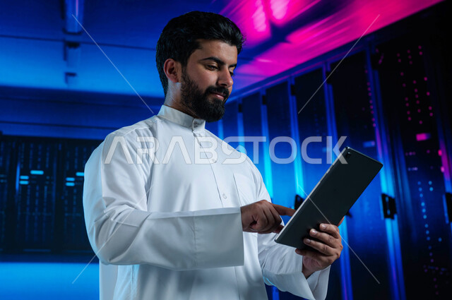 ادارة غرفة التحكم بالسيرفرات وخوادم الانترنت العملاقة، رجل عربي خليجي سعودي يستخدم جهاز التابليت، الاستفادة من الخبرات السعودية في تطوير الداتا سنتر، شبكة التخزين السحابي، خلفية هولوجرامية ثلاثية الأبعاد لمركز البيانات