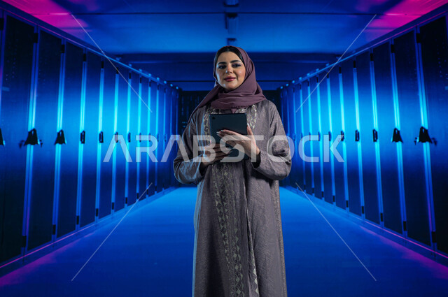 خلفية هولوجرامية ثلاثية الأبعاد لغرفة التحكم بالسيرفرات وخوادم الانترنت، امرأة عربية خليجية سعودية تقوم بإدارة المواقع المستضافة على السيرفرات من خلال جهاز التابلت، مفهوم  تكنولوجيا التخزين السحابي، تسهيل الوصول للمعلومات من خلال نظم قواعد البيانات