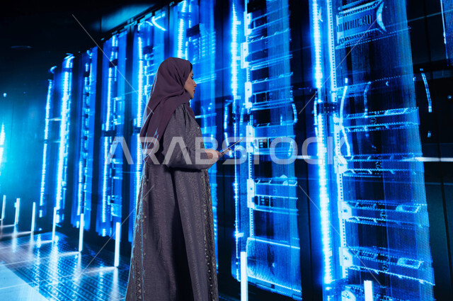 تسهيل الوصول للمعلومات من خلال نظم قواعد البيانات، امرأة عربية خليجية سعودية تقوم بإدارة المواقع المستضافة على السيرفرات من خلال جهاز التابلت، مفهوم  تكنولوجيا التخزين السحابي، خلفية هولوجرامية ثلاثية الأبعاد لغرفة التحكم بالسيرفرات وخوادم الانترنت