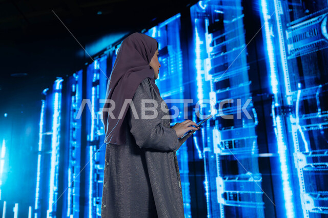 حفظ وتخزين المعلومات لمستخدمين المواقع، امرأة عربية خليجية سعودية تقوم بالإشراف وإدارة بيانات الداتا سنتر باستخدام جهاز التابليت، خوادم الانترنت العملاقة، مفهوم  تكنولوجيا التخزين السحابي، خلفية هولوجرامية ثلاثية الأبعاد لغرفة الخوادم والسيرفرات