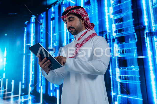 الاستفادة من الخبرات السعودية في تطوير الداتا سنتر، رجل عربي خليجي سعودي يقوم بالإشراف والتحكم في مركز البيانات باستخدام جهاز التابليت، تسهيل الوصول للمعلومات من خلال نظم قواعد البيانات، خلفية هولوجرامية ثلاثية الأبعاد لغرفة الخوادم والسيرفرات