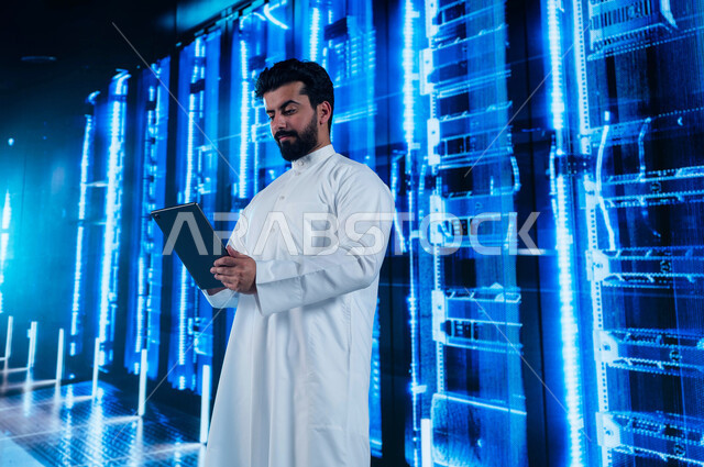 مفهوم تكنولوجيا التخزين السحابي، إستثمار الخبرات السعودية في بناء مراكز بيانات متطورة وحديثة، رجل عربي خليجي سعودي يستخدم جهاز التابليت في الإشراف وإدارة بيانات ومعلومات الداتا سنتر، خلفية هولوجرامية ثلاثية الأبعاد لغرفة الخوادم والسيرفرات