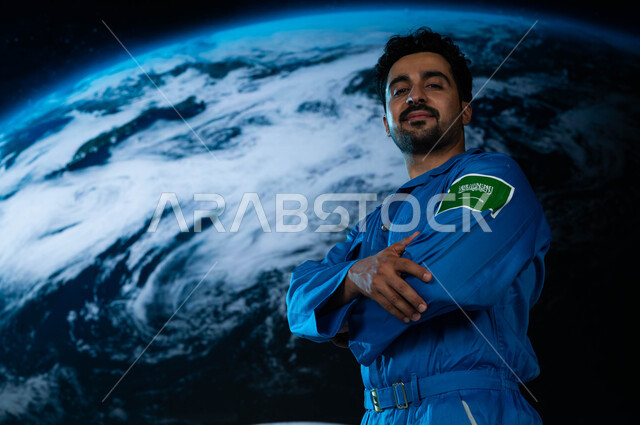 أول رائد عربي خليجي سعودي يصل الى القمر, الوقوف بأيدي متقاطعة, رواد فضاء سعوديين, رحله السعودية الى العالم الفضائي, شعار علم السعودية على البدلة الفضائية الزرقاء, تطور و نمو قطاع الفضاء في الوطن العربي, خلفية هولوجرامية ثلاثية الابعاد لكوكب الأرض.