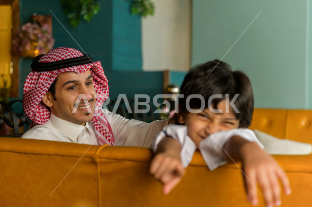 طفل عربي خليجي سعودي يقضي وقته مع والده في المطعم بايماءات و تعابير وجه تدل على السعادة ، قضاء العطلة مع العائلة ، أجواء عائلية ترفيهية ، جلسات فريدة و مميزة ، مطاعم و كافيهات في السعودية