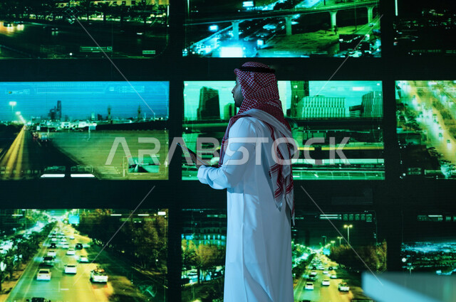  القيام بمراقبة الحركه المروريه في طرق وشوارع مدينة الرياض، خلفية شاشات حديثه ،صورة من الخلف لرجل عربي خليجي سعودي يرتدي الزي التقليدي, كاميرات إلكترونيه متطورة ، مركز الاداره والإشراف على أمن أحياء ومناطق السعوديه، رؤية ٢٠٣٠