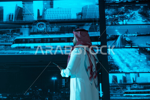  القيام بمراقبة الحركه المروريه في طرق وشوارع مدينة الرياض، خلفية شاشات حديثه ،صورة من الخلف لرجل عربي خليجي سعودي يرتدي الزي التقليدي, كاميرات إلكترونيه متطورة ، مركز الاداره والإشراف على أمن أحياء ومناطق السعوديه، رؤية ٢٠٣٠