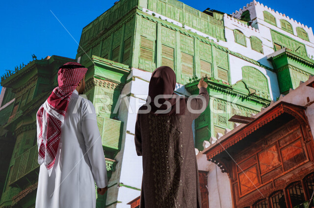 الاشارة الى شيء ما, مناطق سياحية مشهورة, التصميم المعماري العربي القديم, المعالم التاريخية في جدة في حي البلد, صورة من الخلف لرجل و امرأة عربيان خليجيان سعوديان يقومان بالنظر إلى المباني الأثرية في البلد التاريخي في مدينة جدة في المملكة العربية السعودية