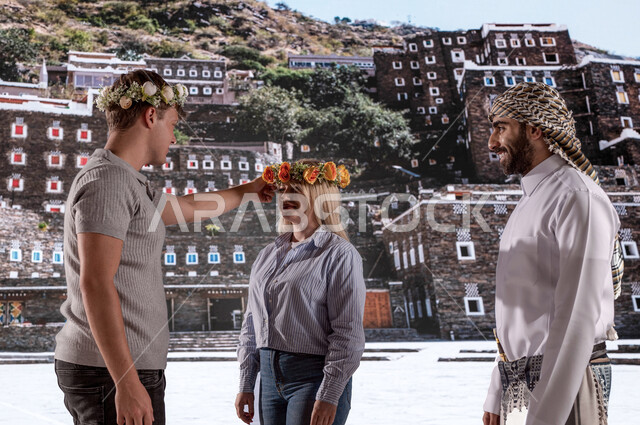  معالم سياحية مشهورة، ايماءات تدل على السعادة, عادات وتقاليد شعبيه ،الوقوف أمام قرية رجال ألمع التراثية في منطقة عسير،الأثار التاريخية القديمة في أبها ،رجل عربي خليجي يرتدي الزي الجنوبي الشعبي مع الزائرين الاجانب يرتدون اكليل من الورد العسيري العطري