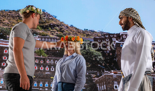 ايماءات تدل على السعادة, عادات وتقاليد شعبيه ،الوقوف أمام قرية رجال ألمع التراثية في منطقة عسير،الأثار التاريخية القديمة في أبها ،رجل عربي خليجي يرتدي الزي الجنوبي الشعبي مع الزائرين الاجانب يرتدون اكليل من الورد العسيري العطري, معالم سياحية مشهورة