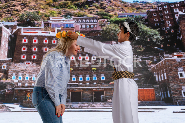 Popular customs and traditions in wearing a wreath of fragrant Asiri roses, the arrival of tourists from all over the world, standing in front of the ancient historical monuments and houses in Abha, a Gulf Arab boy wearing the southern folk costume with a