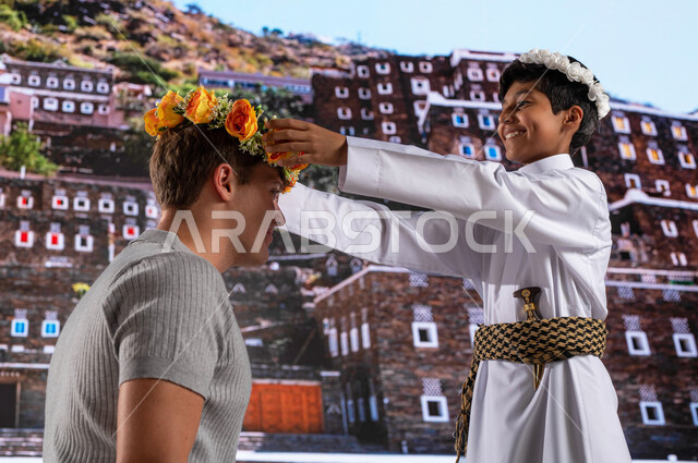 الأثار و البيوت التاريخية القديمة في أبها ،ولد عربي خليجي مبتسم يرتدي الزي الشعبي الجنوبي مع سائح أجنبي يقفون أمام قرية رجال ألمع التراثية في منطقة عسير, عادات وتقاليد شعبيه في ارتداء اكليل من الورد العسيري العطري , معالم ومناطق سياحية مشهورة