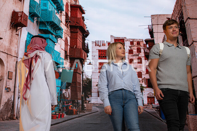 معالم ومناطق  سياحيه تاريخيه مشهوره في السعودية، صورة من الخلف لرجل سعودي مع السائحين الاجانب يتجولون بين الأحياء الشعبيه و المباني الأثرية في جده التاريخيه, الرواشين الخشبيه في البناء المعماري العربي القديم  في حي البلد, الدليل السياحي للسياح