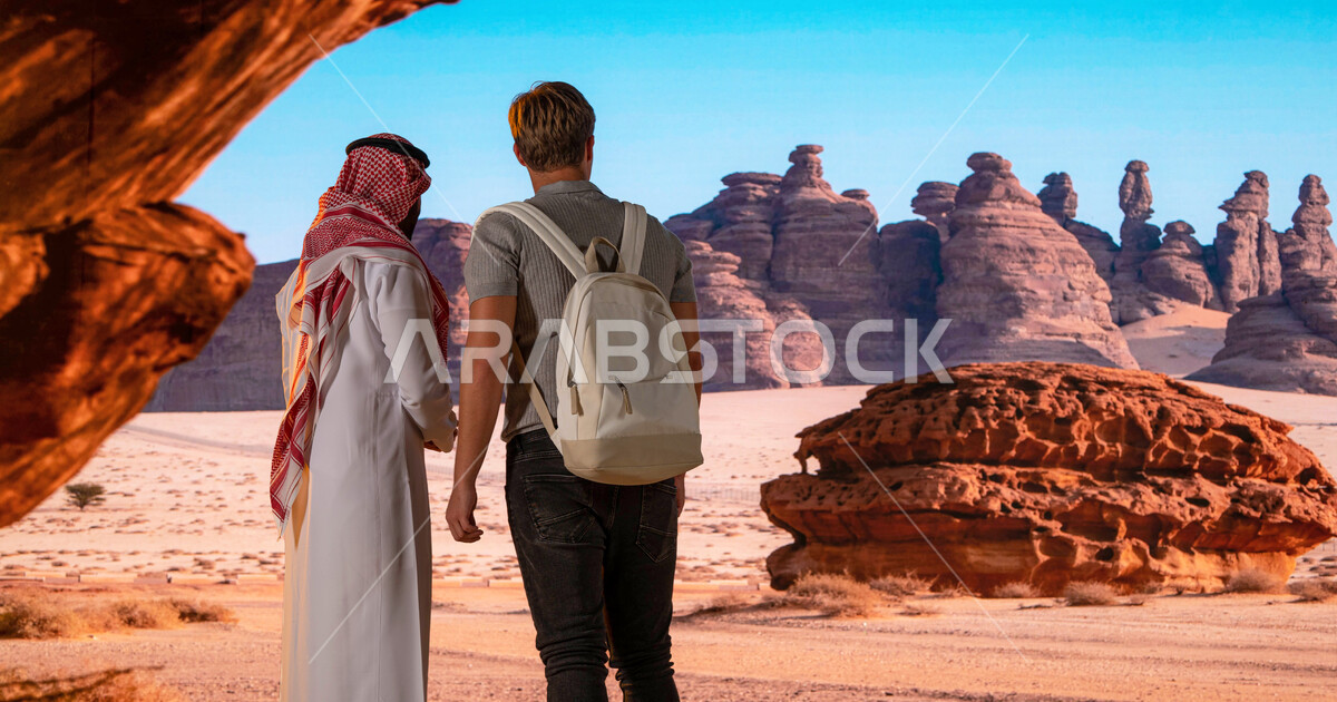صورة من الخلف لزائر اجنبي مع رجل عربي سعودي يقفان امام القمم والمرتفعات 