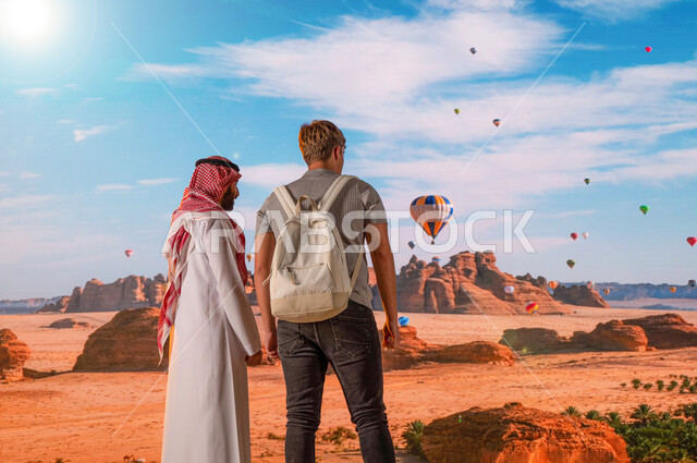 فتح أبواب السياحة السعودية، المناطيد في سماء المملكة في محافظة العلا, الطيران في بالون الهواء الساخن, الدليل السياحي للسياح، صورة من الخلف لرجل عربي خليجي يرتدي الزي السعودي التقليدي مع سائح أجنبي يقومان بفعاليات و أنشطه ترفيهيه, معالم أثرية تاريخية قديمة