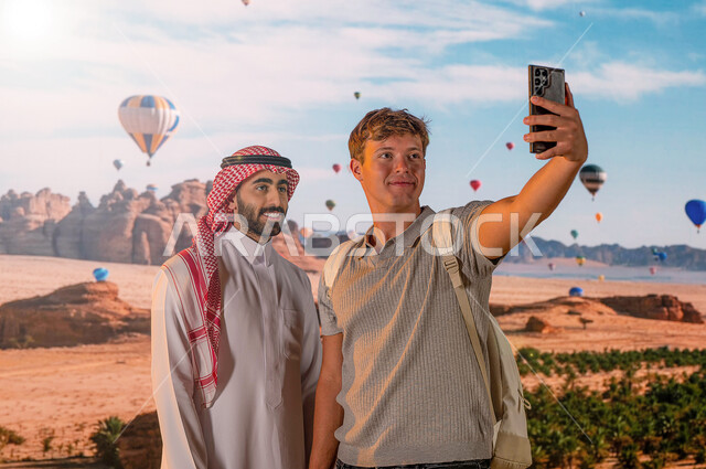 الطيران في بالون الهواء الساخن, الدليل السياحي للسياح، موقع أثري في اليونسكو, انشطه وفعايلات ترفيهيه ، رجل عربي خليجي يرتدي الزي السعودي التقليدي مع سائح أجنبي يقوم بالتقاط صور السيلفي التذكارية عبرالجوال ، معالم أثرية تاريخية قديمة، وجهه سياحية طبيعيه