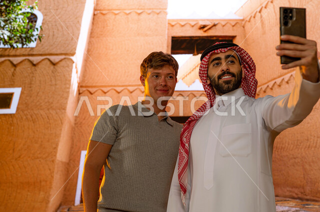 رحلات تعليميه ثقافية سياحية, معالم تاريخية وطنية ,صورة مقربة لسائح أجنبي مع الدليل السياحي السعودي  يرتدي الزي التقليدي يقوم بالتقاط صور السيلفي التذكارية عبر الجوال, الوقوف في المتحف الوطني التاريخي في مدينة الرياض, مركز الملك عبد العزيز (قصر المربع)