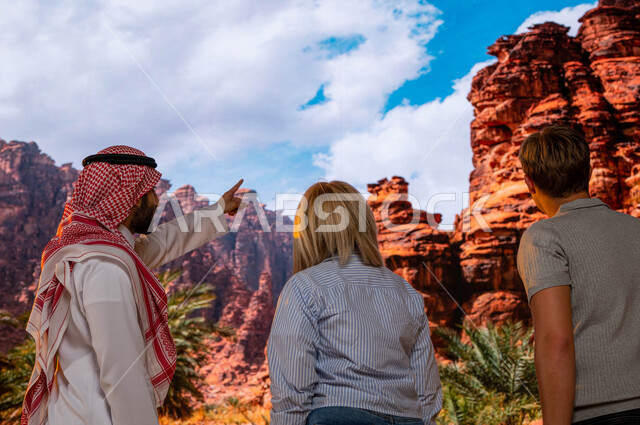 صورة مقربة من الخلف لزائرين اجانب مع مرشد سياحي سعودي يقف في منطقة العلا في السعودية و الاشارة الى شيئ ما , فتح أبواب السياحة السعودية، الدليل السياحي للسياح، الطبيعه الجبلية المتميزة في المعالم الأثرية التاريخيه السياحيه المشهوره, وجهه سياحية طبيعيه