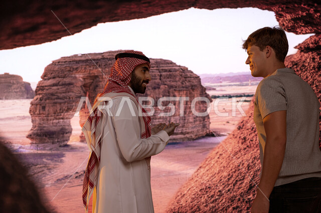 قدوم الزائرين من شتى أنحاء العالم، معالم سياحيه أثرية في محافظة العلا في السعوديه, صورة مقربة لسائح أجنبي مع الدليل السياحي يقومان بتبادل الأحاديث والنقاشات أمام جبل الفيل الصخري في الطبيعه الجبلية المميزة في مدينة العلا، فتح أبواب السياحة السعودية