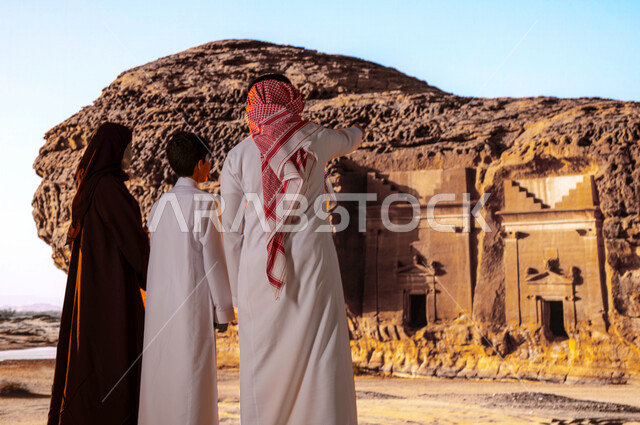 المعالم التاريخيه الاسلامية البارزه في مدائن صالح في العلا، قضاء وقت ممتع مع الابناء في الأماكن القديمة الأثرية، انشطه ترفيهيه عائلية سياحية في السعودية, صورة من الخلف لعائلة عربية خليجية سعودية تقف أمام التشكيلات و التكوينات الصخرية والاشارة إلى شيء ما