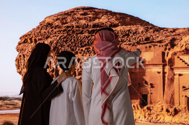المعالم الاسلاميه التاريخيه  البارزه  في مدائن صالح في العلا، قضاء وقت ممتع مع الابناء في الأماكن القديمة الأثرية، انشطه ترفيهيه عائلية سياحية, صورة مقربة من الخلف لعائلة عربية خليجية سعودية تقف أمام التشكيلات و التكوينات الصخرية والاشارة إلى شيء ما