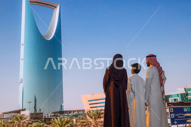 An educational family trip, the architectural engineering art of towers and skyscrapers, urban growth and development, a back view of a Saudi Arabian Gulf family looking at the Kingdom Tower in the city of Riyadh in Saudi Arabia, recreational activities a