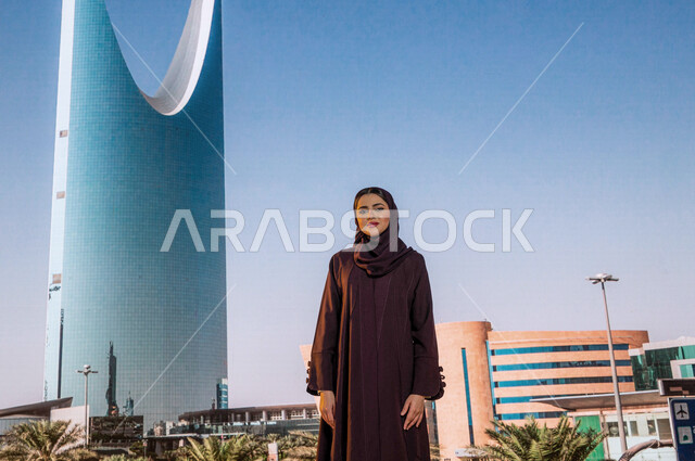 Famous tourist areas, urban development and growth, the Kingdom Tower in the city of Riyadh in Saudi Arabia, the architectural engineering art of towers and skyscrapers, a smiling Saudi Arab Gulf woman wearing the Gulf abaya and looking at the camera with